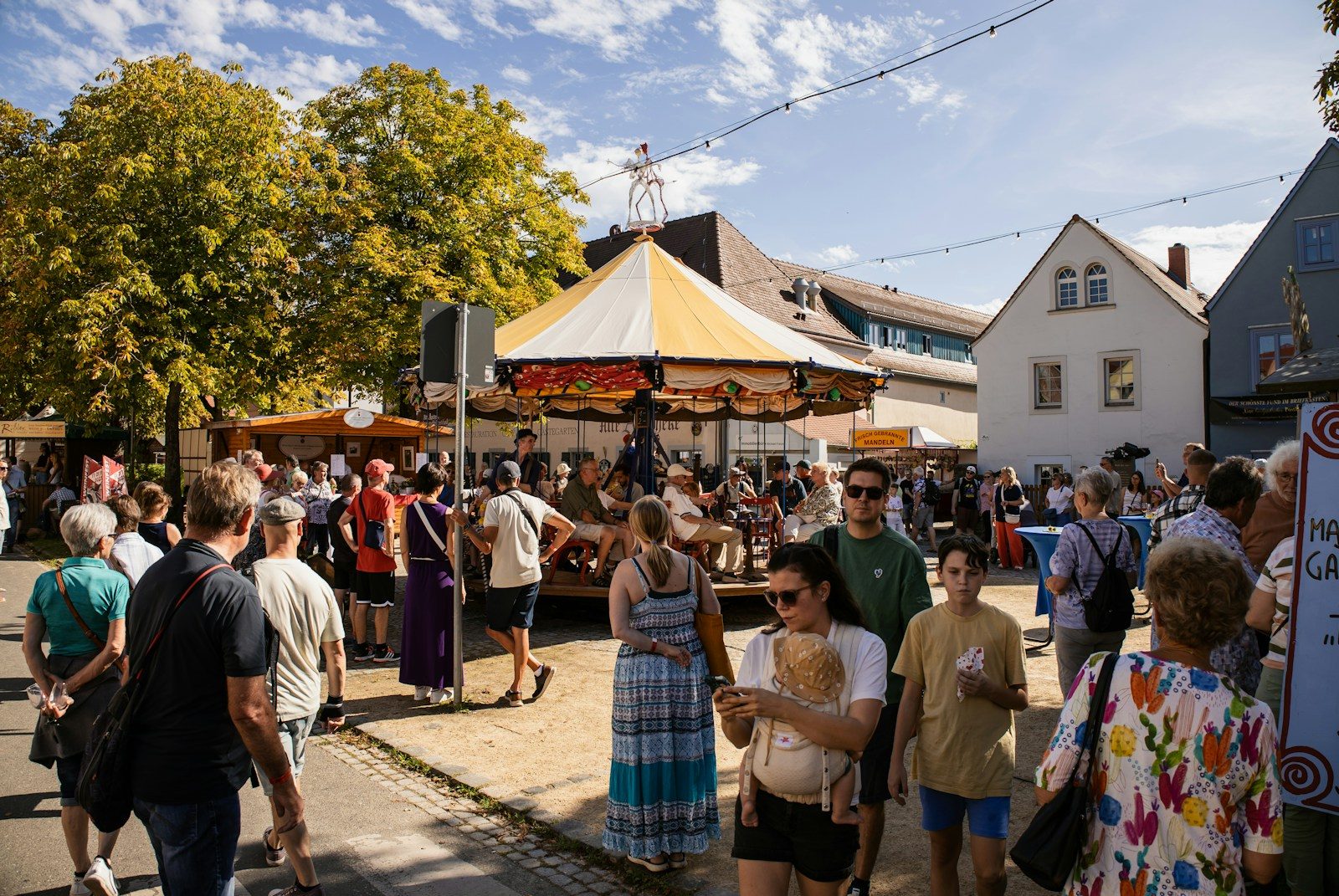 Crowd of people at an outdoor festival with a carousel.